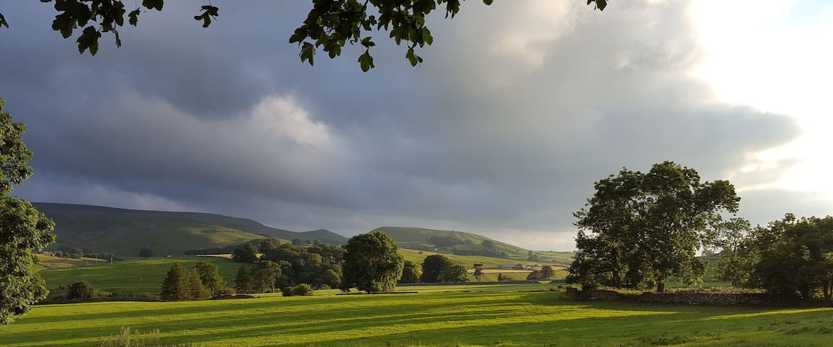 A rural landscape with rolling hills, a stone wall, and a wooden fence.