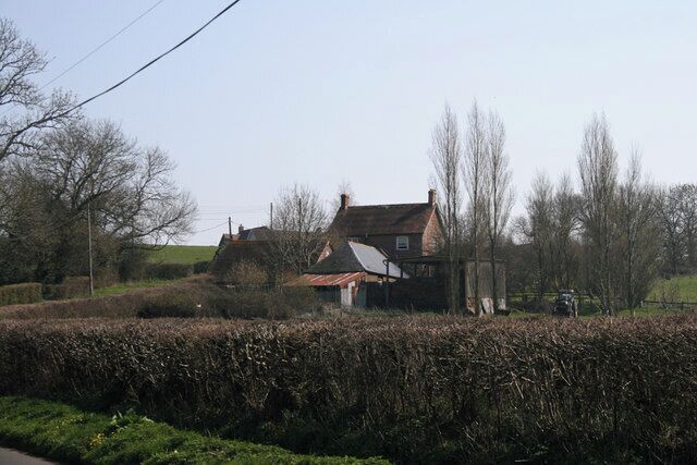 A rural landscape with a house surrounded by hedges and trees.