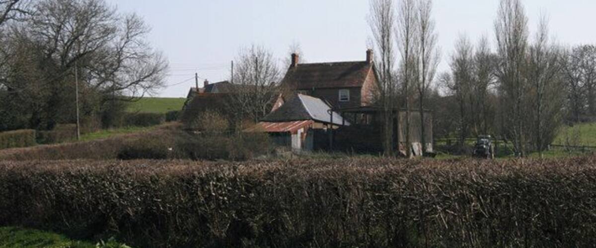 A rural landscape with a house surrounded by hedges and trees.