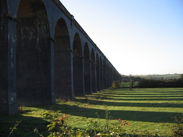 Un largo viaducto de ladrillo con múltiples arcos sobre un campo cubierto de hierba.