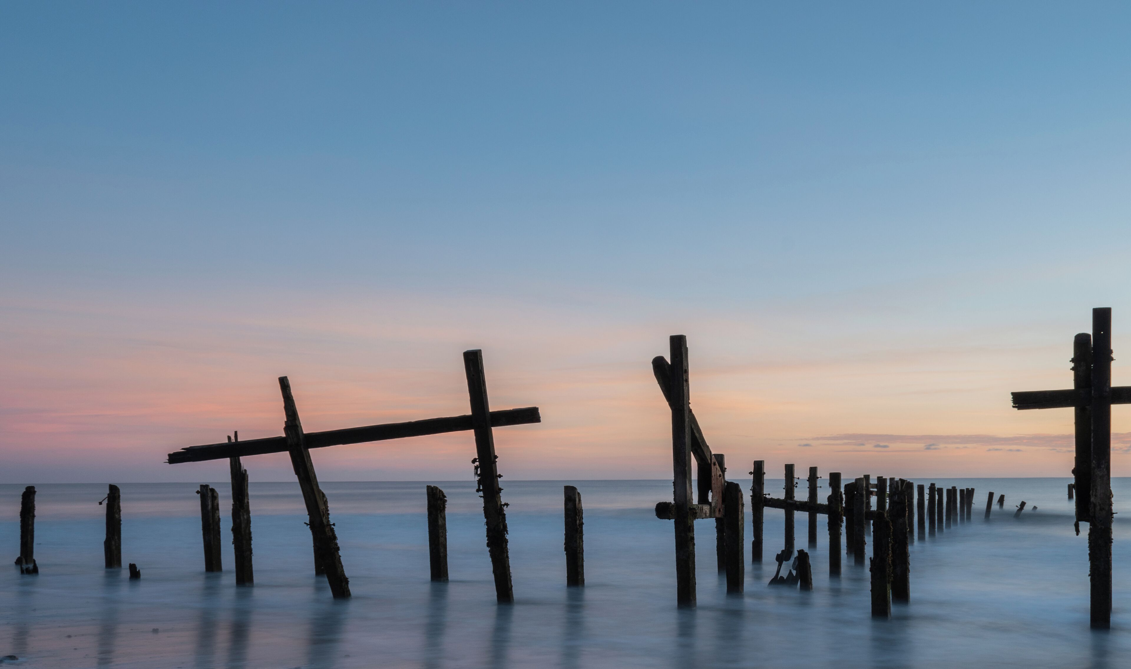 A coastal scene with wooden posts extending into the water at sunset.