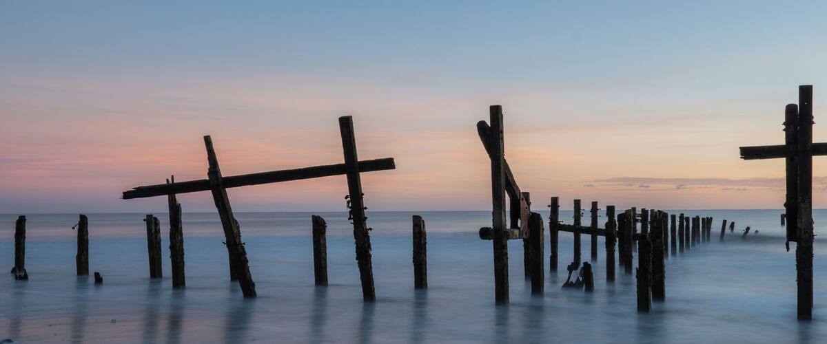 A coastal scene with wooden posts extending into the water at sunset.