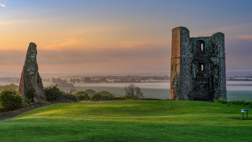 A historic stone tower and ruins on a grassy hill overlooking a misty coastal landscape.