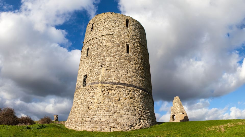 A stone tower with a smaller ruin in the background, set against a cloudy sky.