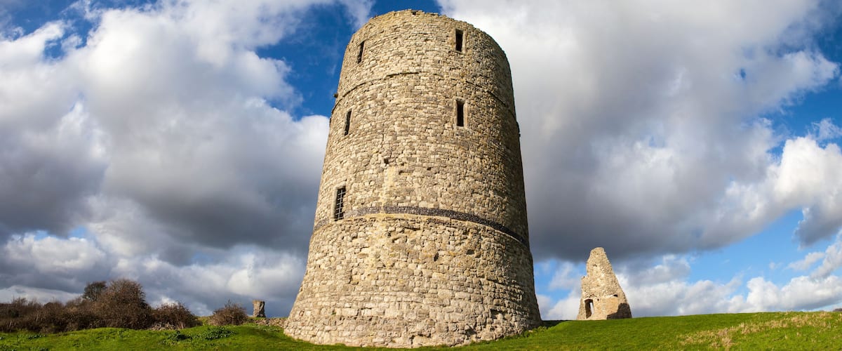 A stone tower with a smaller ruin in the background, set against a cloudy sky.