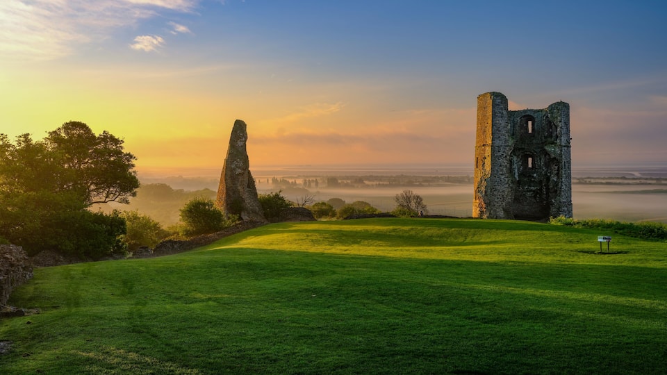 A grassy field with ancient stone ruins and a standing stone in the distance.