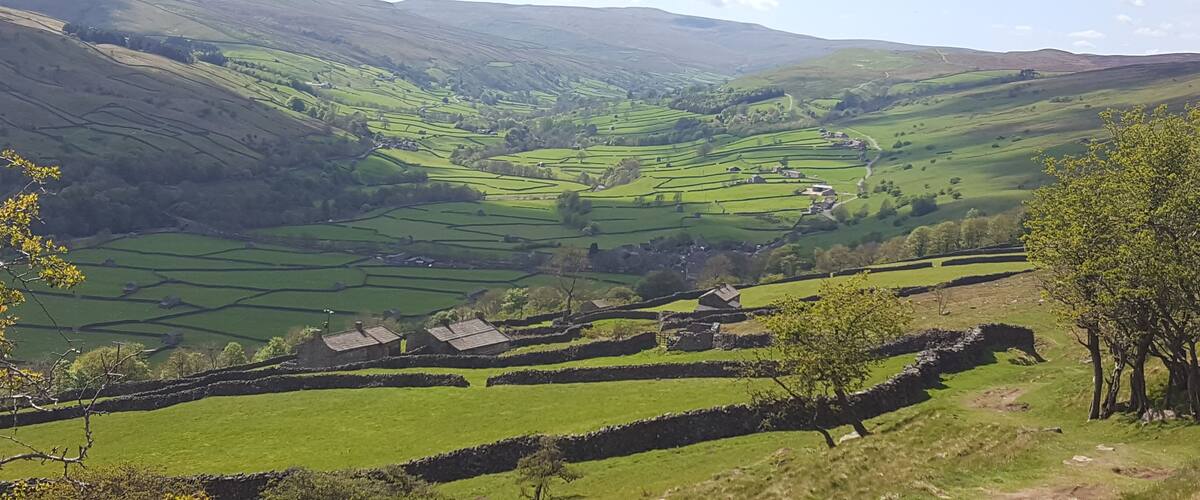 Rolling green hills, stone walls, and scattered houses in a valley.