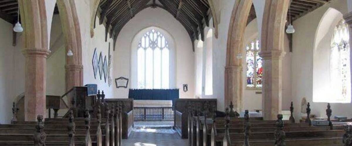 An interior of a church with wooden pews, arched ceilings, and stained glass windows.
