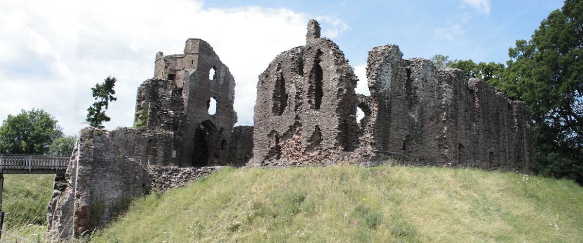 A historic stone ruin with arches and a bridge in the background.