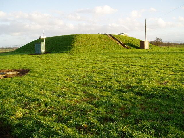 A grassy hill with a small building and a wind turbine.
