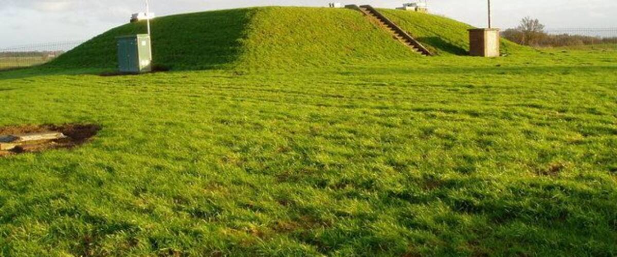 A grassy hill with a small building and a wind turbine.