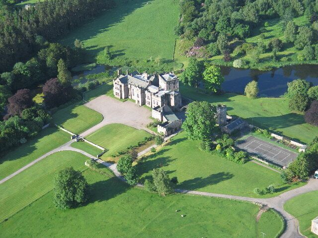 An aerial view of a large estate with a castle-like building, a lake, and well-maintained lawns.