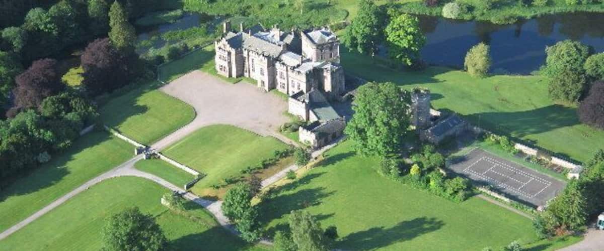 An aerial view of a large estate with a castle-like building, a lake, and well-maintained lawns.