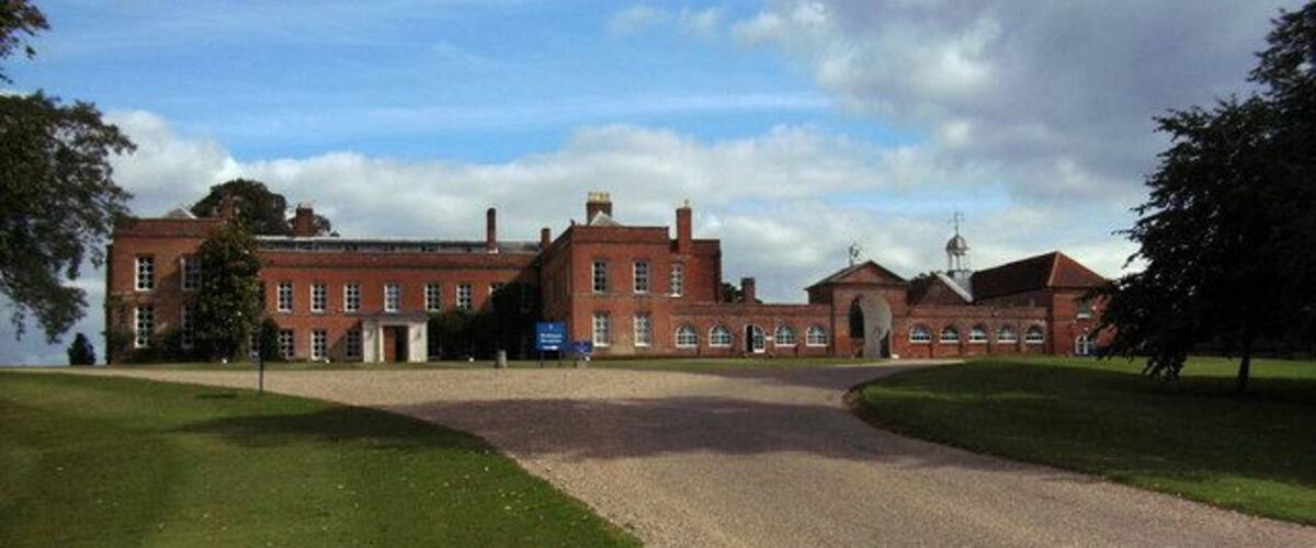 A large red brick building with a gravel driveway leading to a gate.