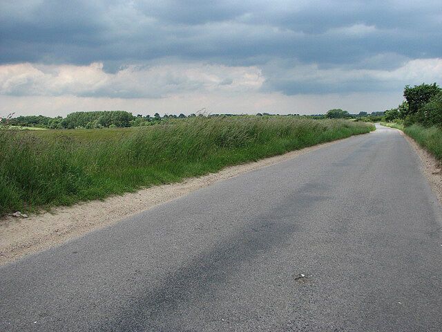 Uma estrada rural com campos gramados e céu nublado.
