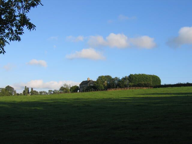 A grassy field with a large building and trees in the background.