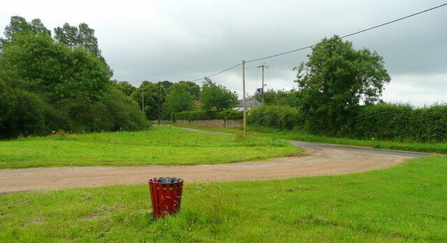 A rural road curving through a green landscape with a red trash bin in the foreground.