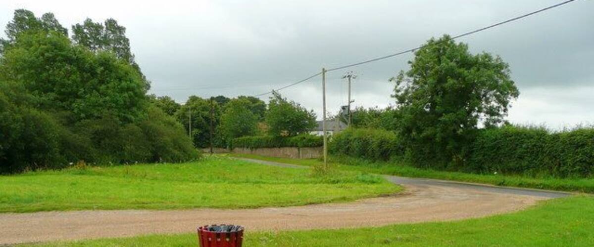 A rural road curving through a green landscape with a red trash bin in the foreground.