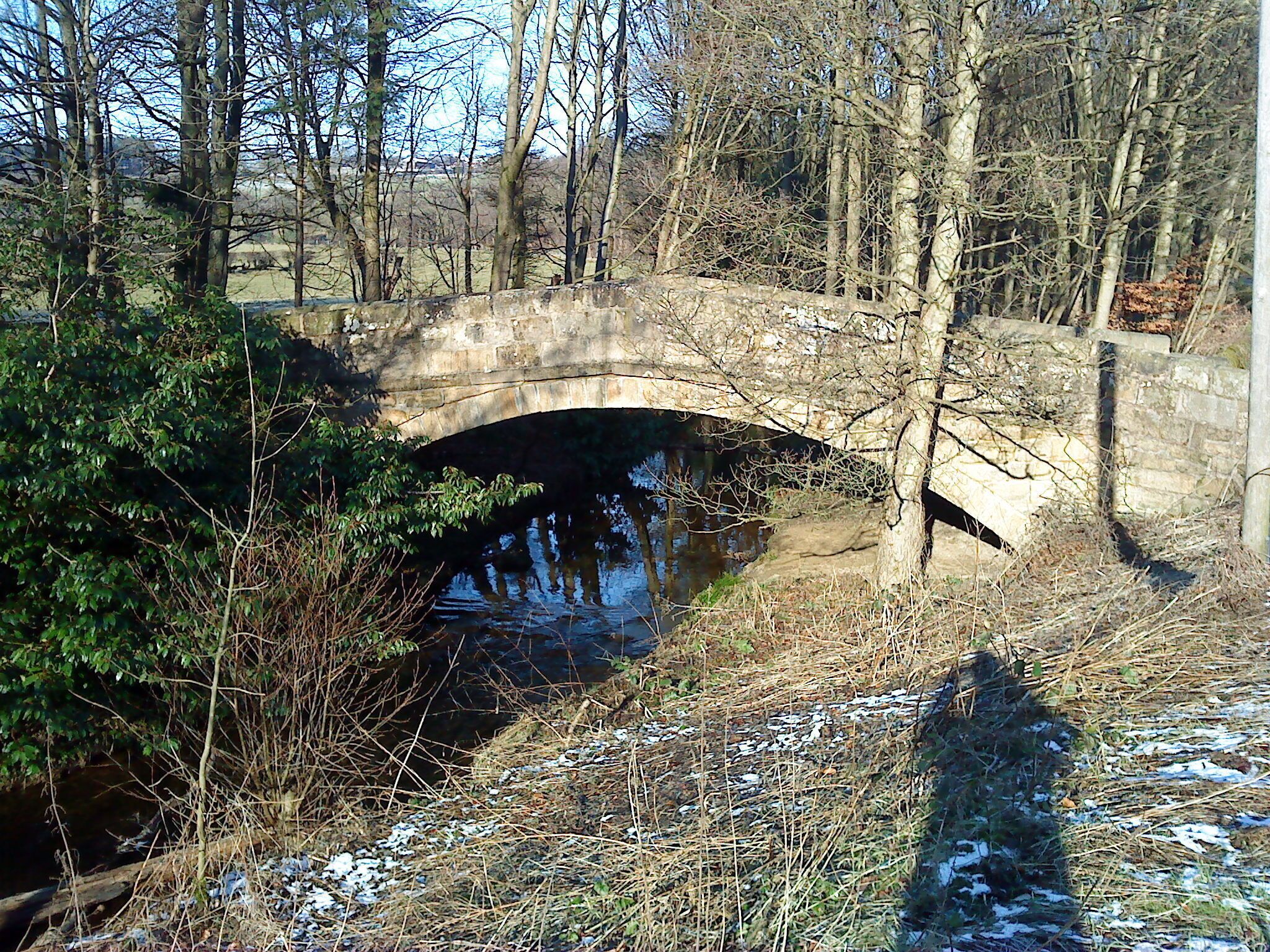 A stone bridge over a narrow waterway, surrounded by trees and bushes.