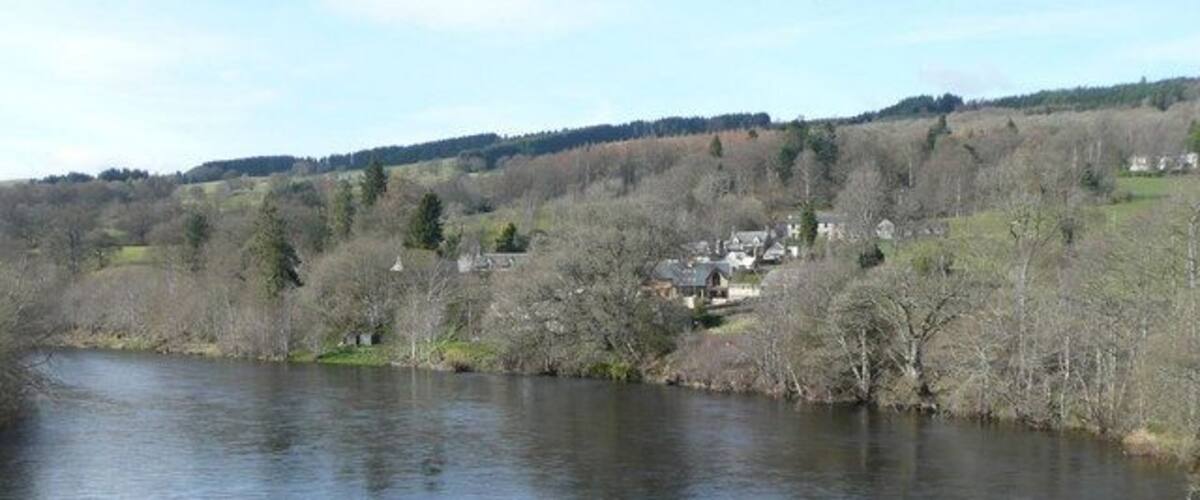 A river with a town on the opposite bank, surrounded by hills and sparse trees.