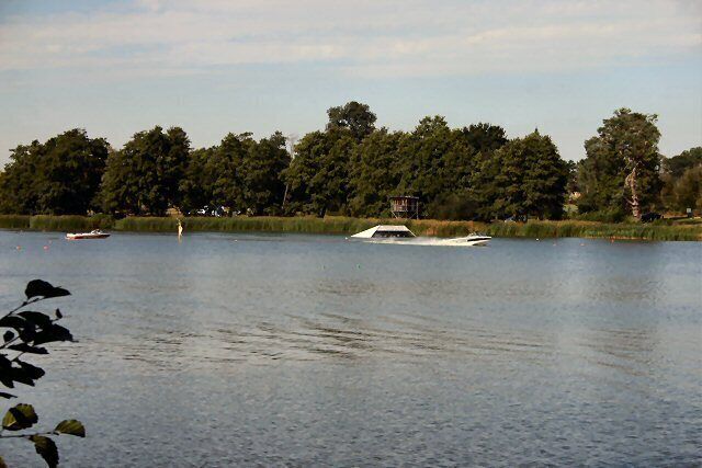 A calm lake with boats, trees, and a dock.