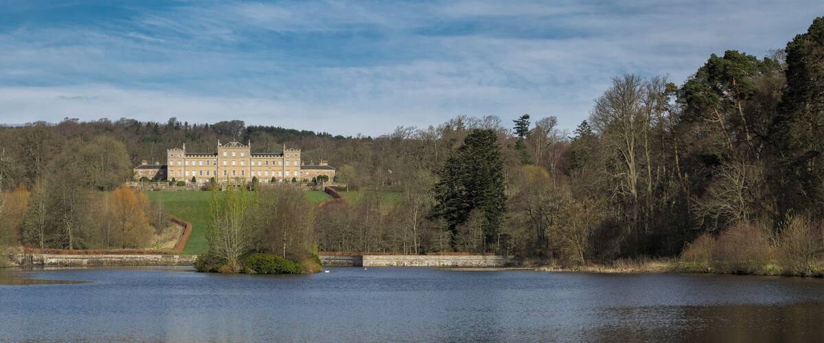 A large stately home surrounded by a lake and forest.