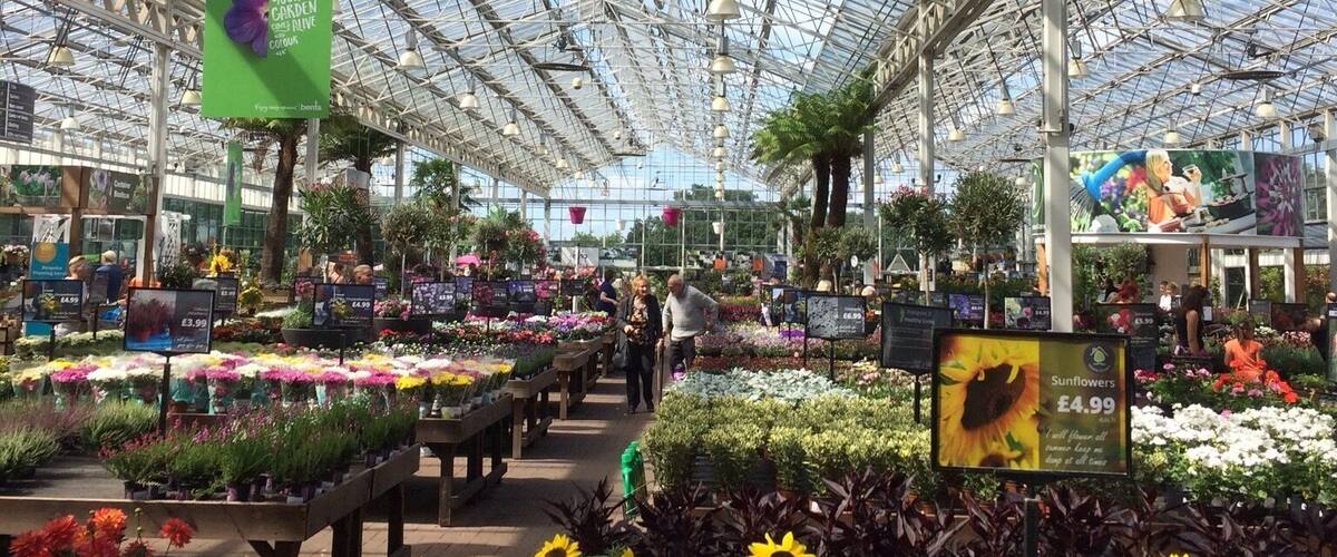 A greenhouse with a glass ceiling, various plants, and price signs.