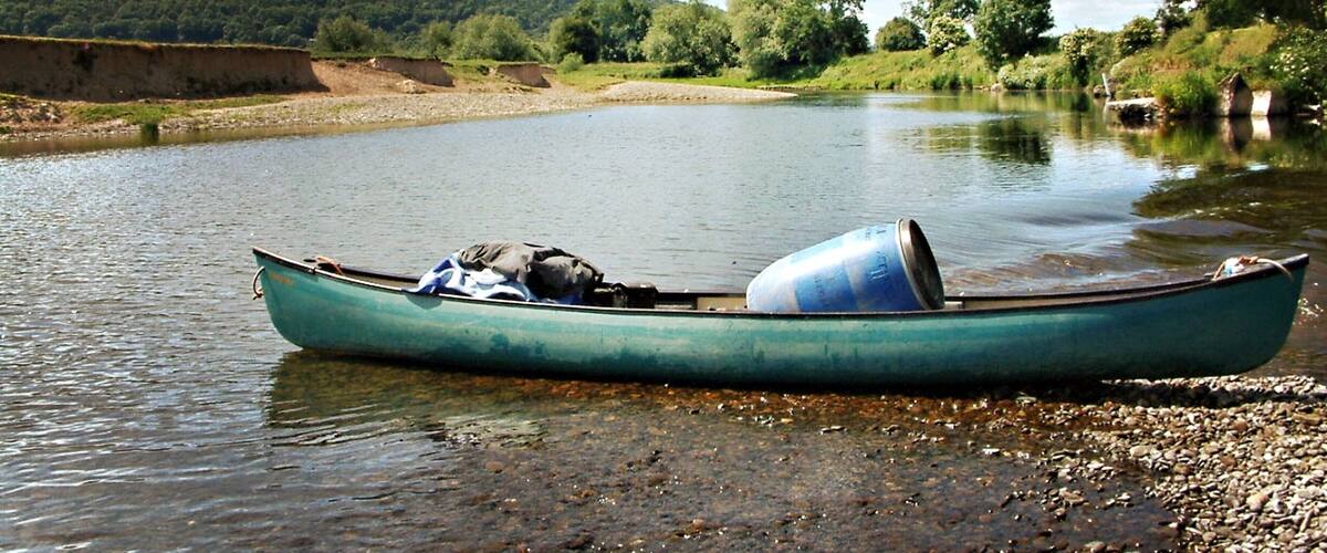 A green canoe on a calm river with a forested hillside in the background.
