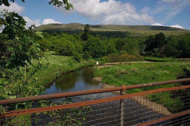 A river flowing through a lush valley with a bridge in the foreground.
