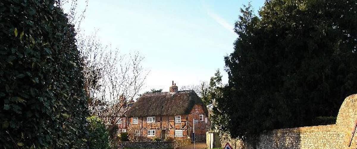 A narrow rural road flanked by stone walls and a thatched-roof house.