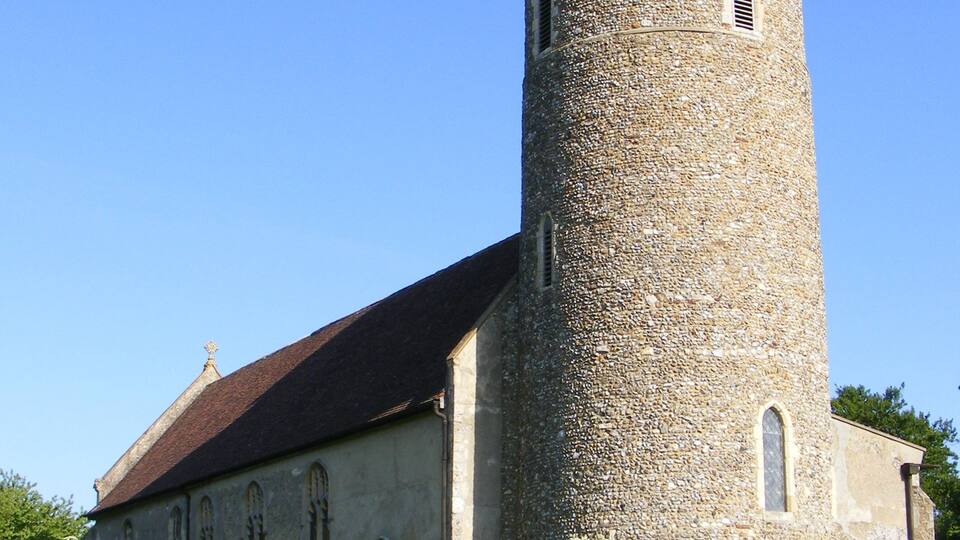 A historic stone church with a tall tower and a brick wall in front.