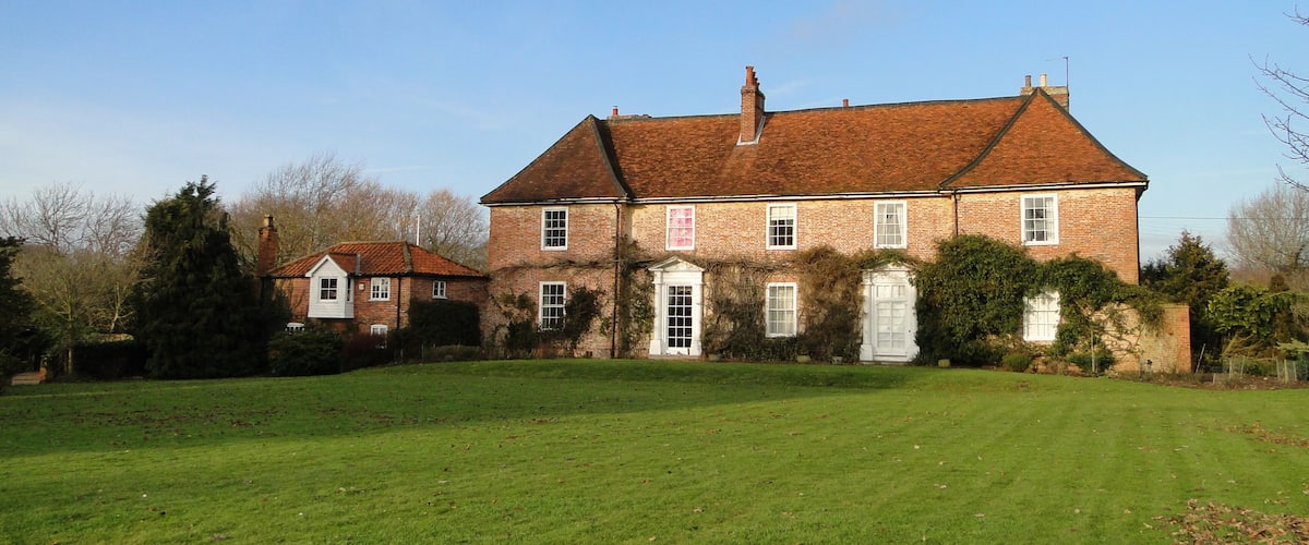 A large brick house with a red roof, surrounded by a well-maintained lawn and trees.