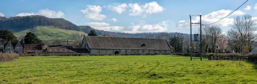 A rural landscape with a large barn, green fields, and a mountain in the background.