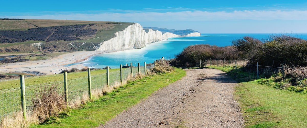 A coastal landscape with white cliffs, a sandy beach, and a clear blue sea.