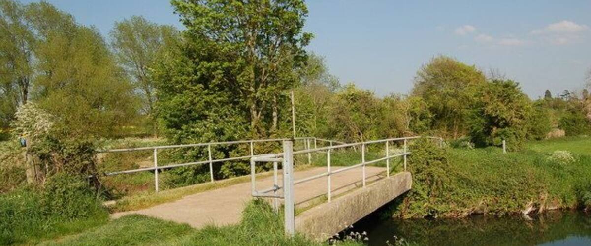 A concrete bridge over a calm river, surrounded by lush greenery and trees.