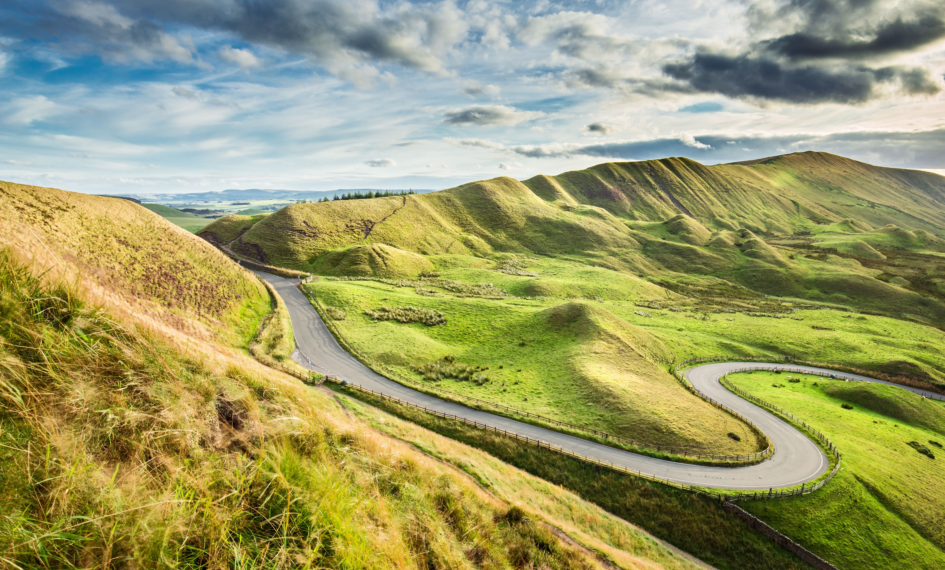 A winding road through rolling green hills under a partly cloudy sky.