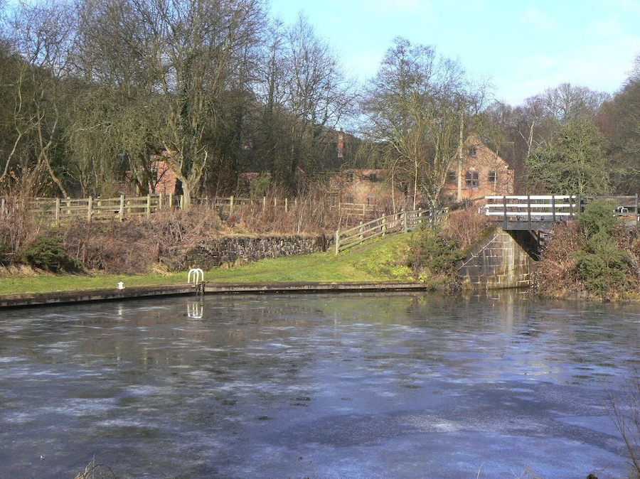 Un río congelado con un puente de madera y edificios de piedra al fondo.