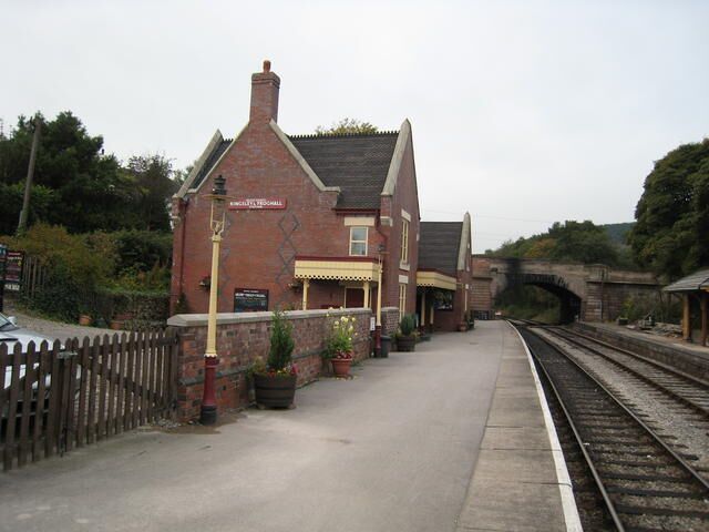 A railway station with a brick building, a platform, and tracks.