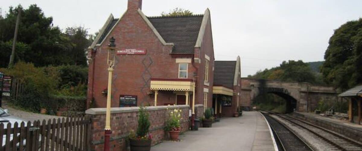 A railway station with a brick building, a platform, and tracks.