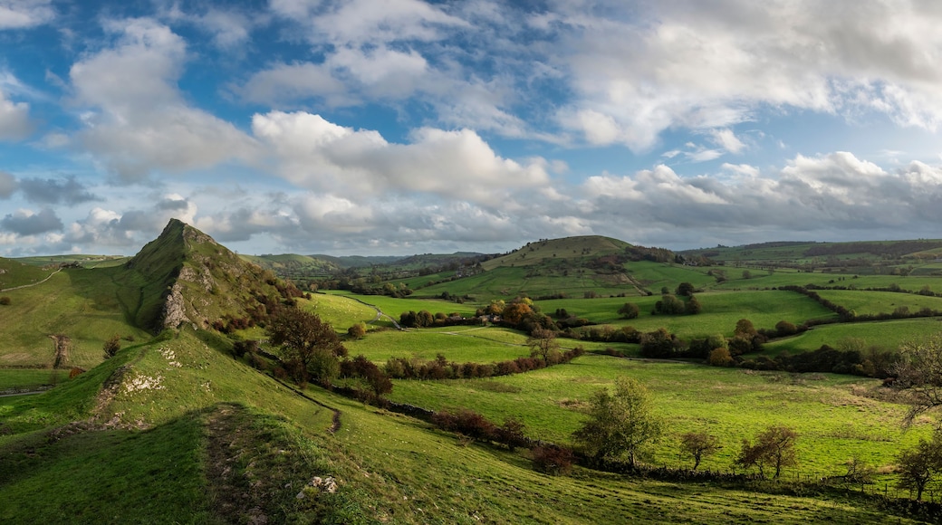 Rolling green hills, a prominent rocky peak, and a winding road.