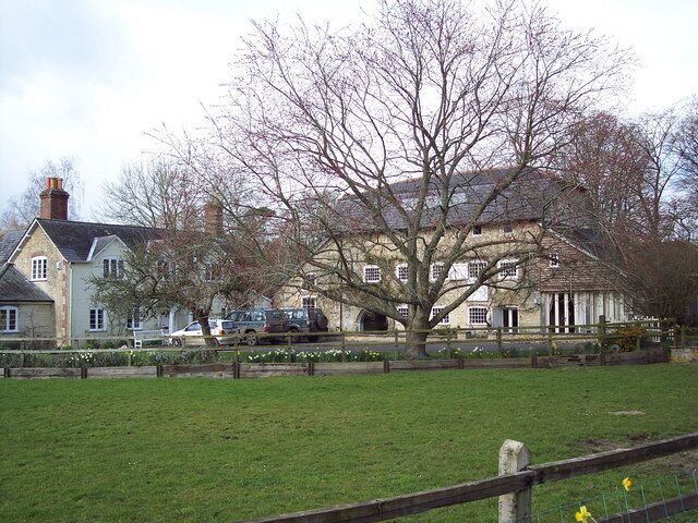 A large estate with a prominent tree in the foreground, a field, and a building with multiple windows and a chimney.