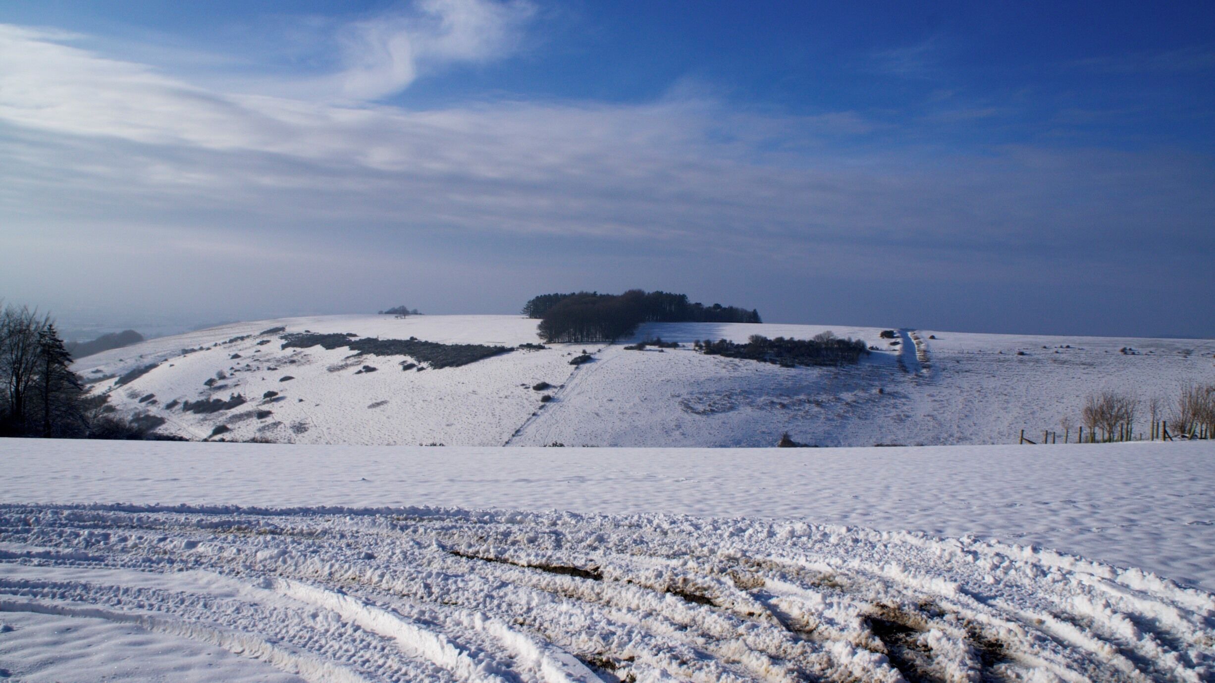 A snow-covered landscape with a forested hill and a clear sky.