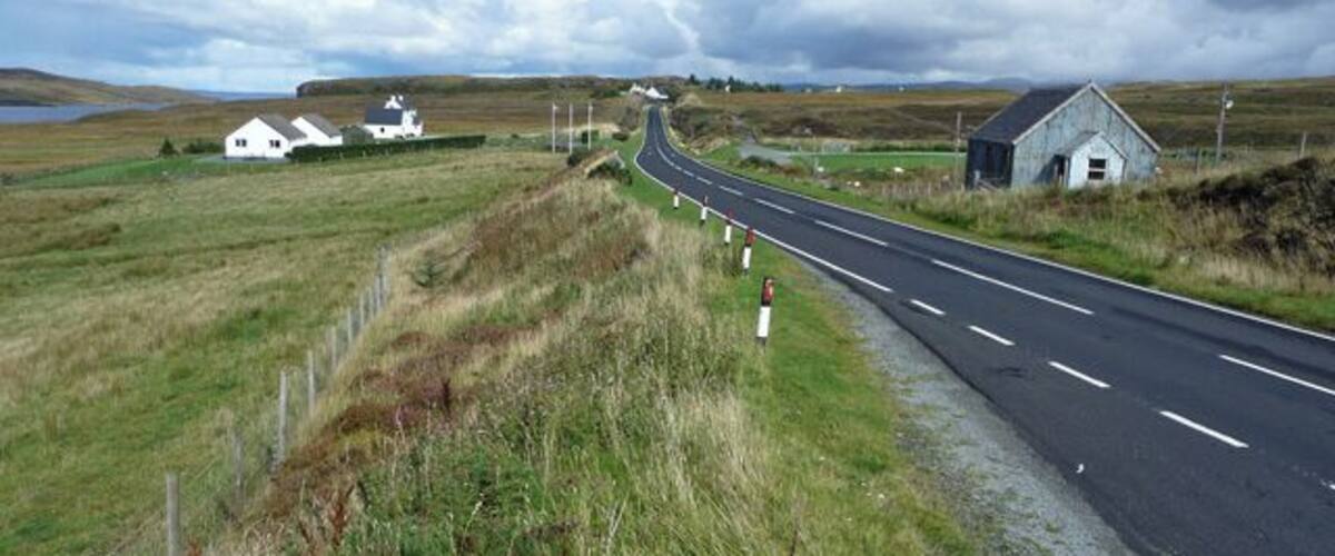 A rural road with houses and a small building on the side.
