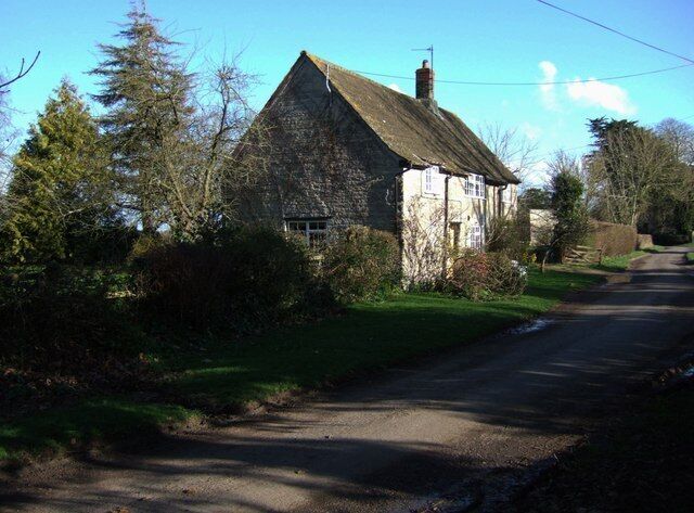 A rural road with a stone house on the left, surrounded by trees and greenery.