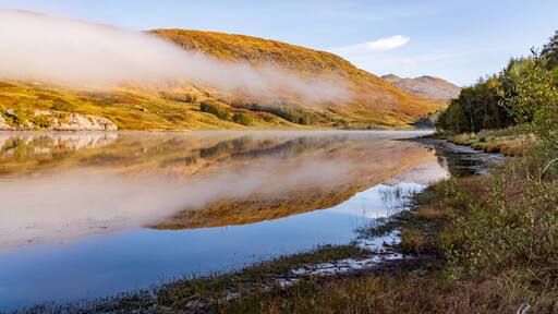 A calm lake reflecting the surrounding hills and a clear sky.
