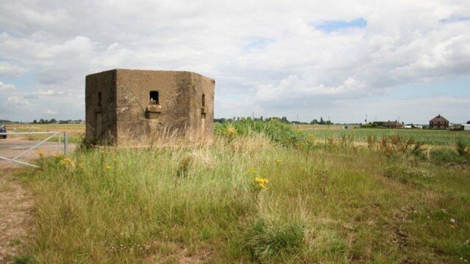 A solitary, weathered structure in a grassy field with a rural backdrop.