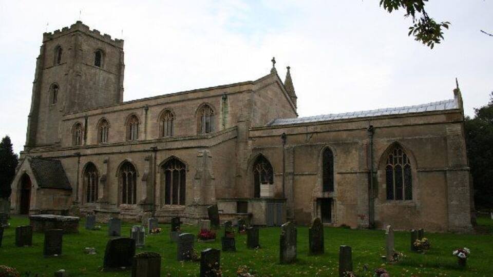A historic church with a tall tower and arched windows, surrounded by a cemetery with headstones and flowers.