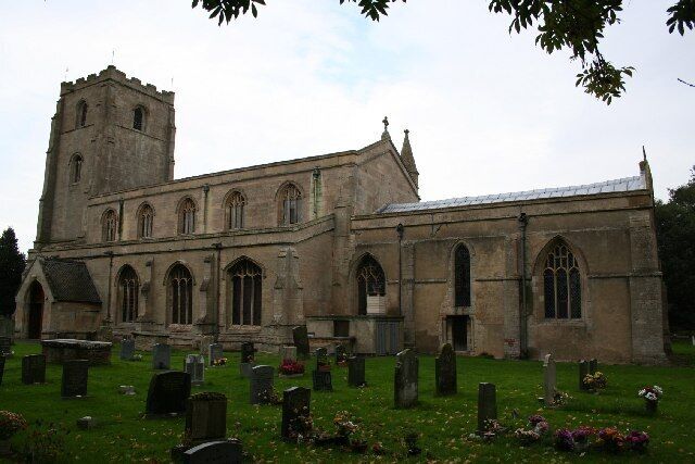 A historic church with a tall tower and arched windows, surrounded by a cemetery with headstones and flowers.