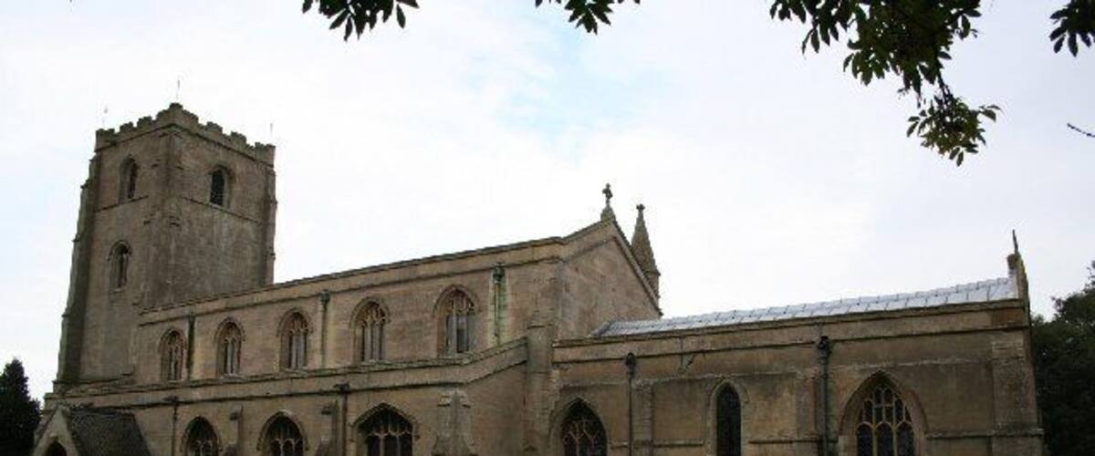 A historic church with a tall tower and arched windows, surrounded by a cemetery with headstones and flowers.