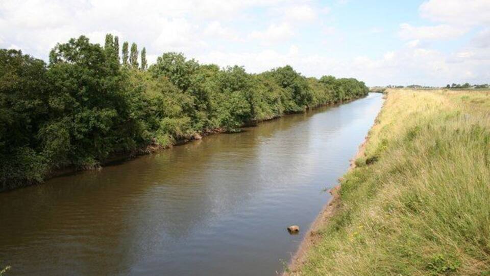 A river flanked by dense greenery and a clear sky.